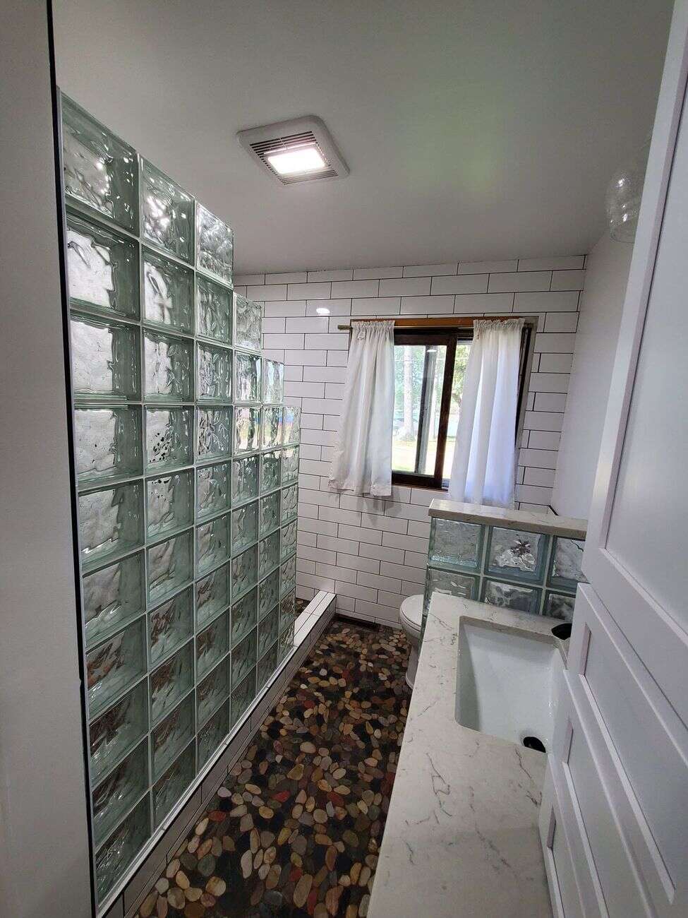 Bathroom with glass block shower wall, white subway tile and river rock floor
