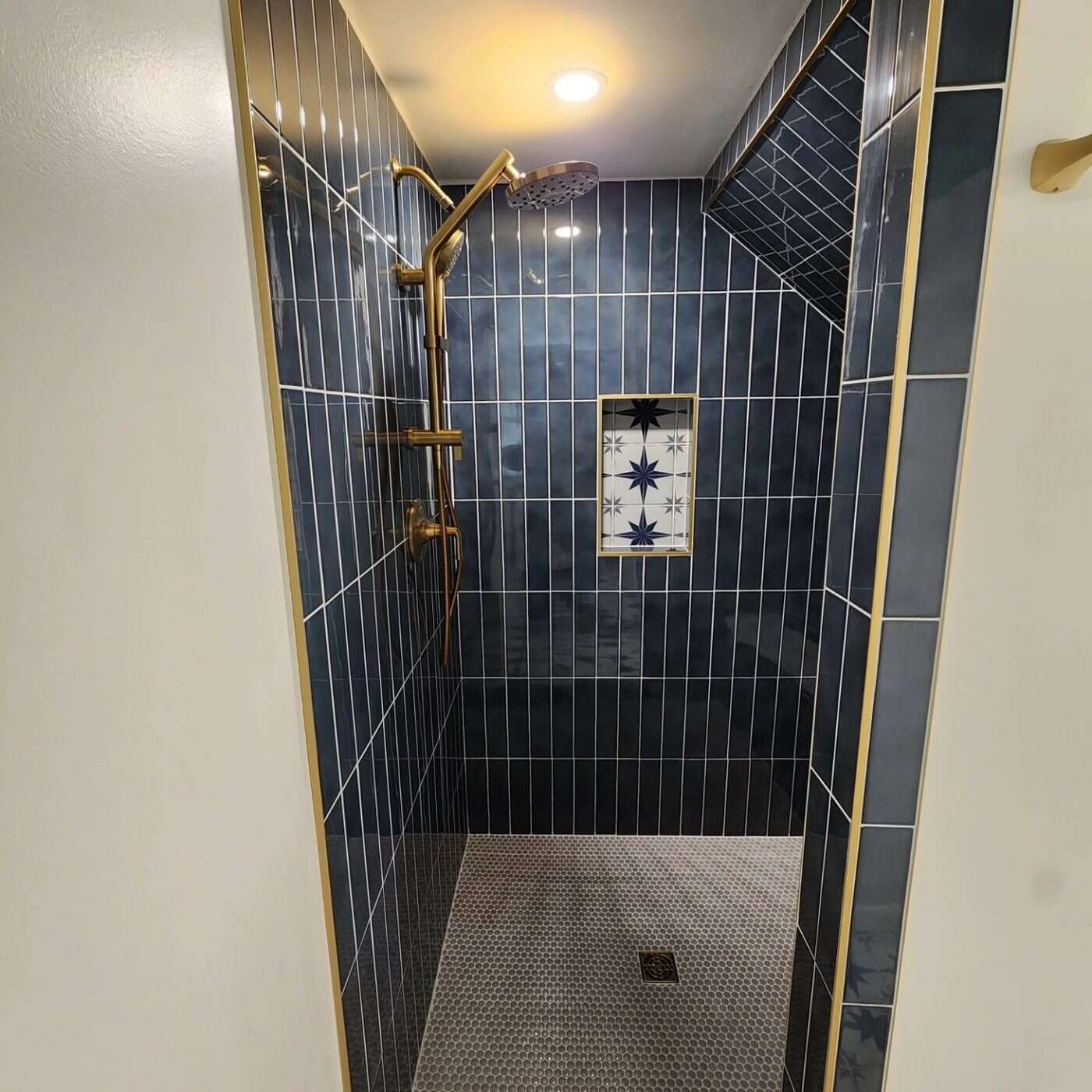 Detail of navy vertical-stack tile shower with brass trim and star mosaic niche