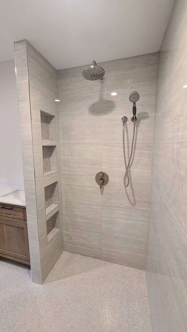 Walk-in shower in travertine-look tile with four stacked hex-lined niches