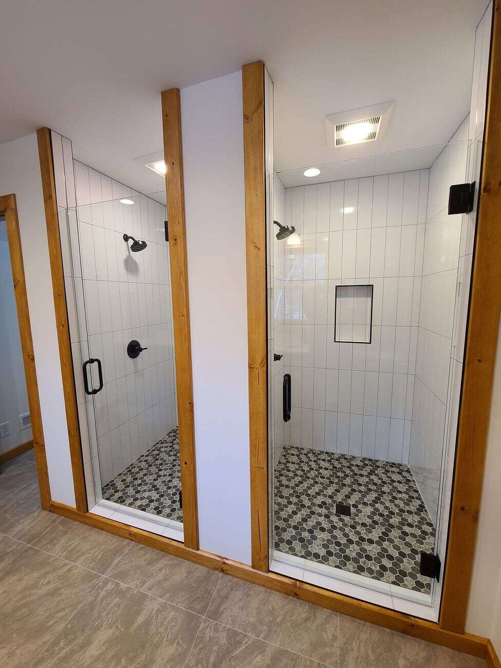 Twin side-by-side glass showers with vertical white tile and hex mosaic floors