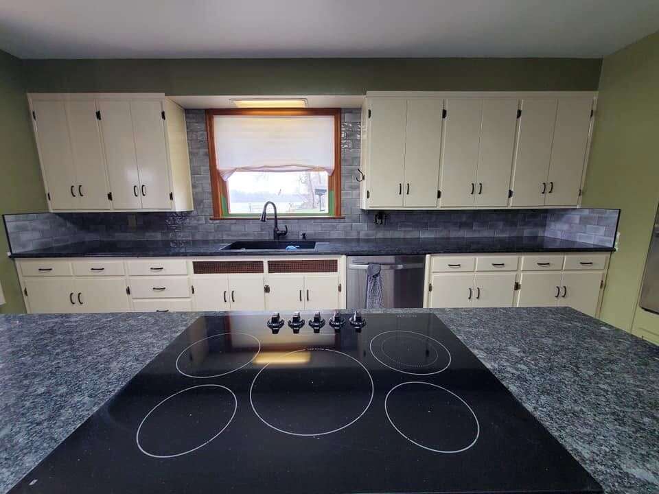 Kitchen with grey subway tile backsplash above dark granite counters