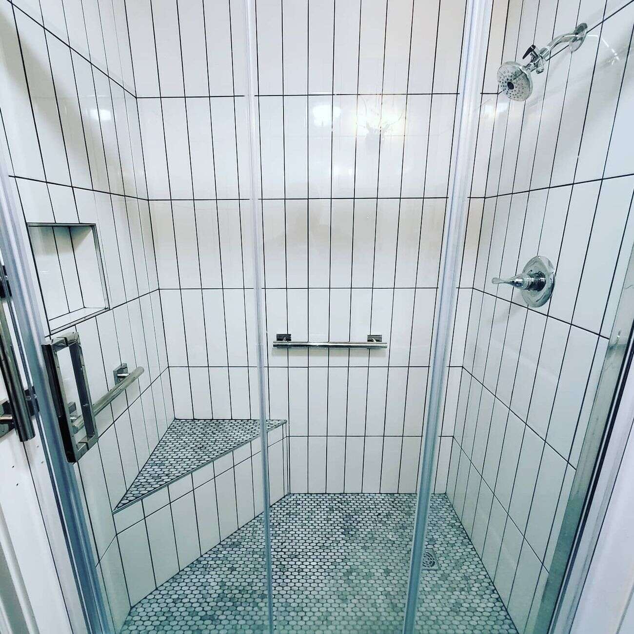 White vertical tile walk-in shower with penny-round floor and bench